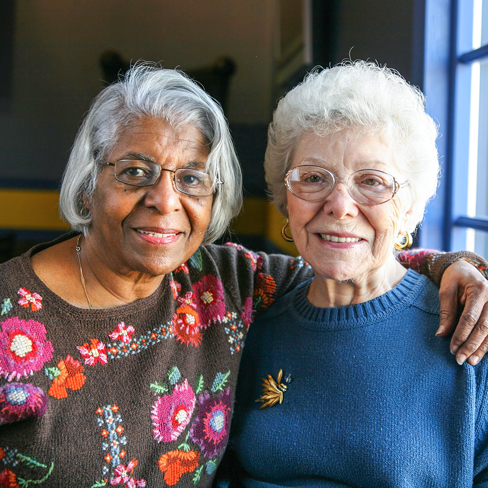 Two elderly women smiling and embracing in a cozy setting.