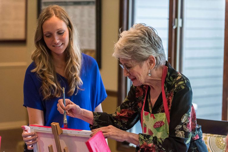 Senior resident painting with staff assistance.