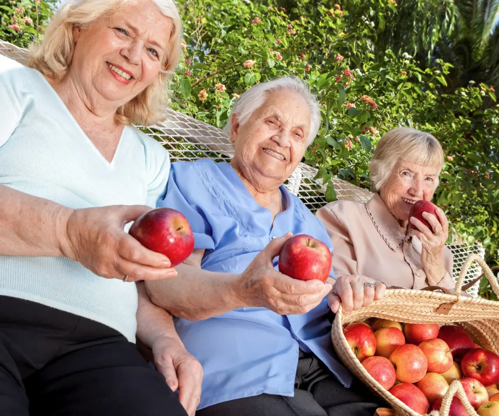 Three seniors enjoying apples outdoors
