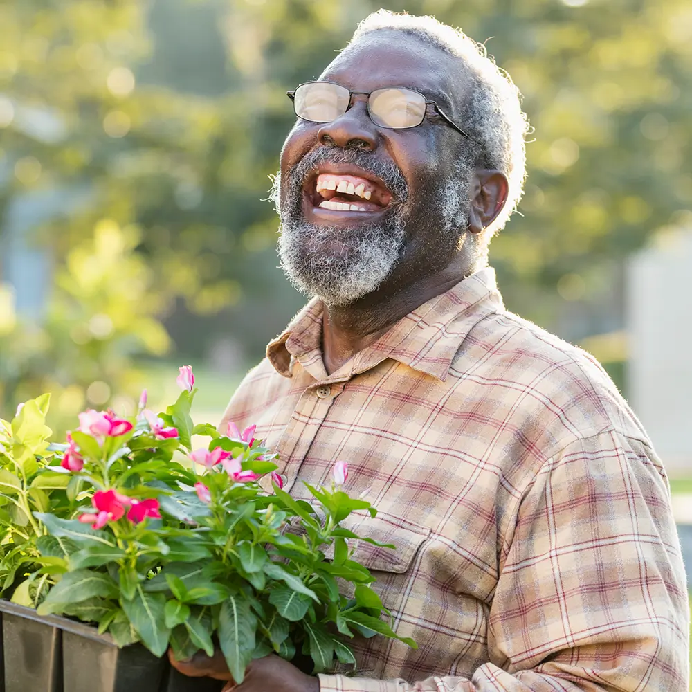 Elderly man smiling with flowers in a garden.