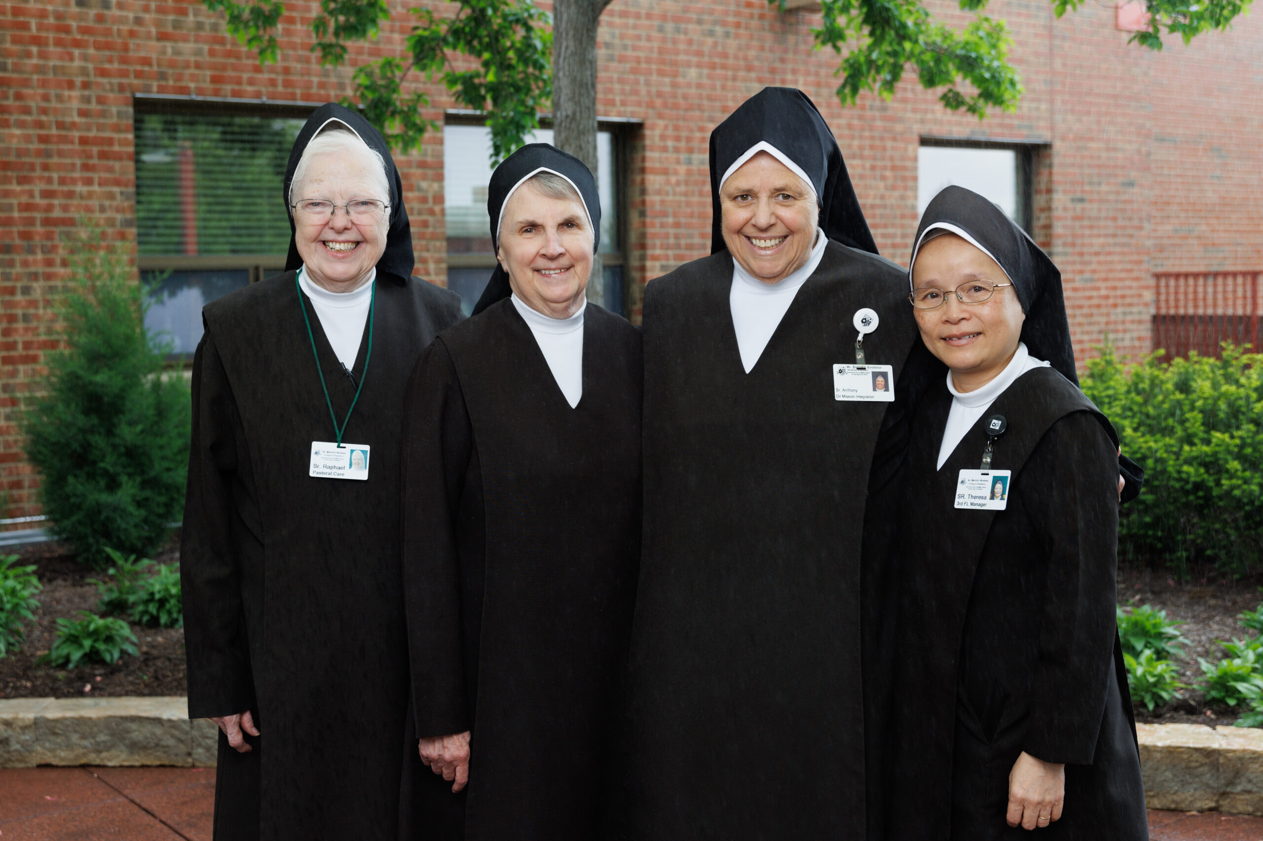 Four nuns in professional attire smiling outdoors