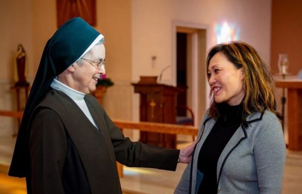 Two women interacting in a serene interior space.
