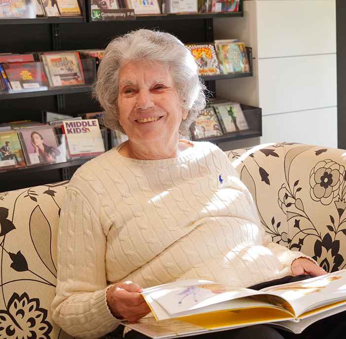 Senior resident reading in a cozy common area.