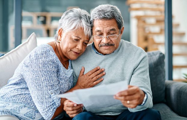 Elderly couple reading a document together on a sofa.