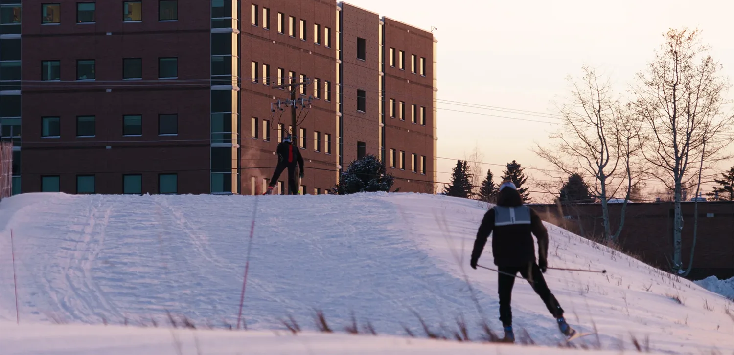 Two people skiing in front of a senior living facility