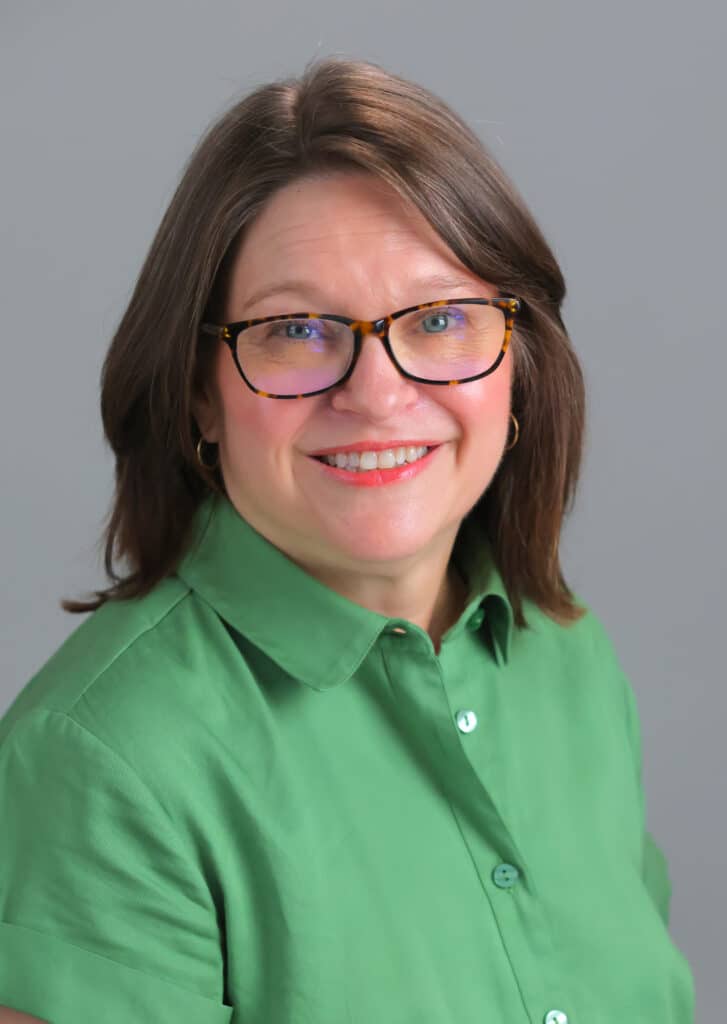 A woman smiling in a green shirt with glasses