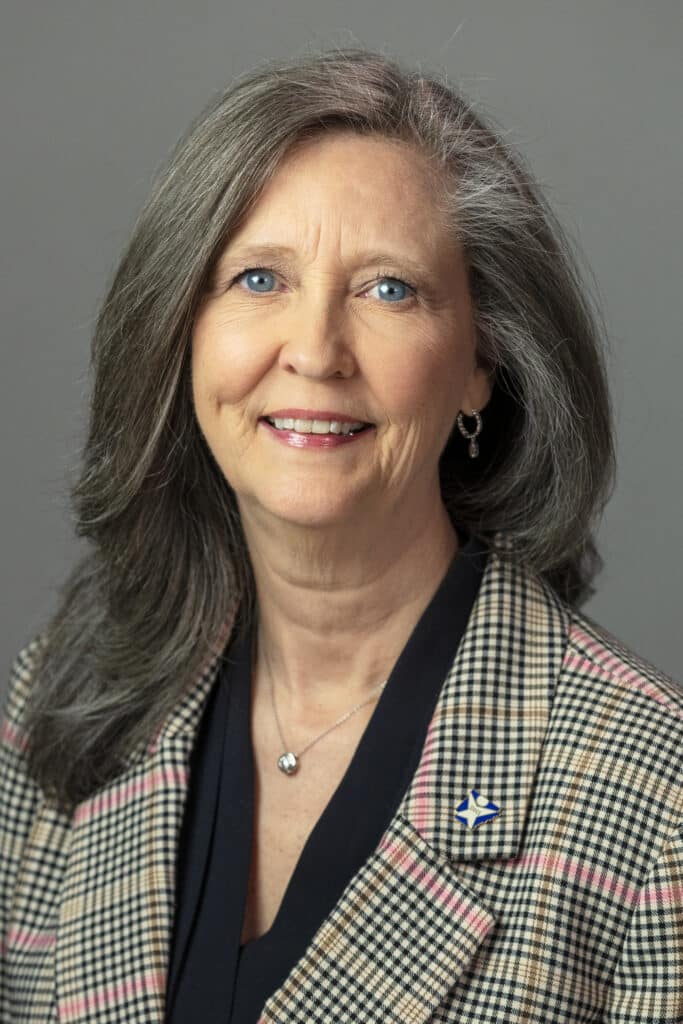 A smiling woman with gray hair wearing a blazer
