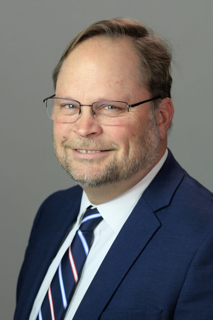 A man in a suit with glasses smiling