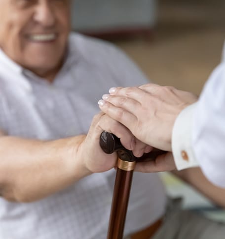 An elderly man smiling while holding a cane with staff's hands on top