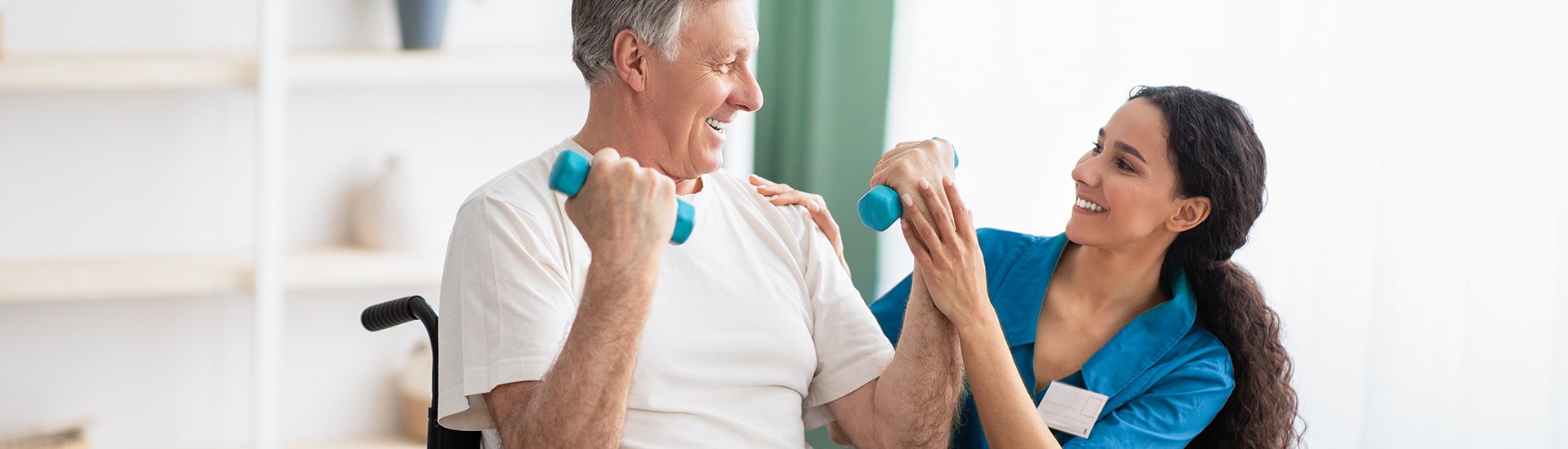 A caregiver assisting a senior man with weights in a bright room