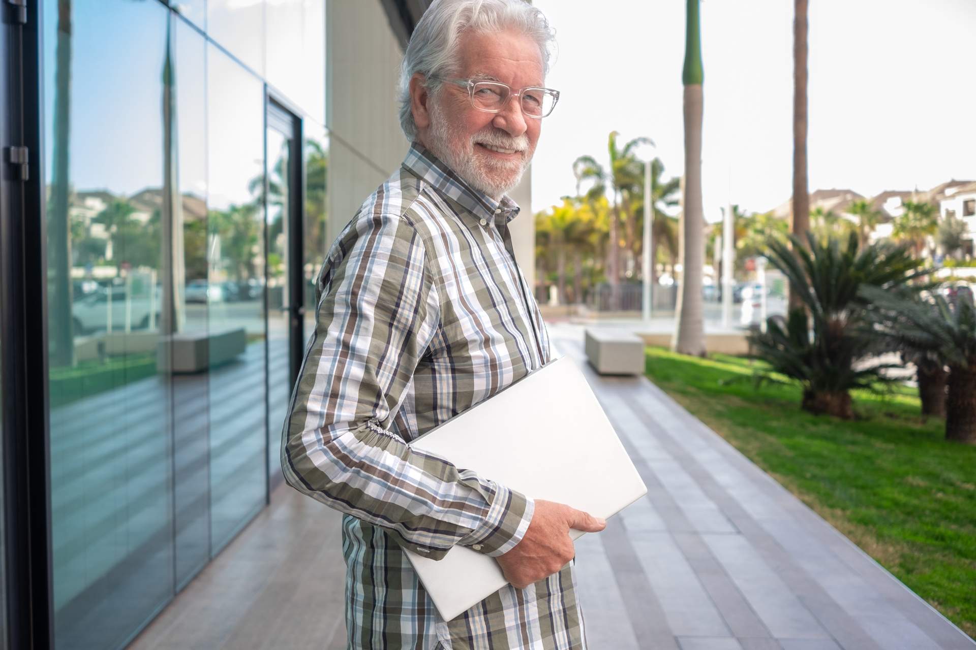 A smiling senior man holding a laptop outside