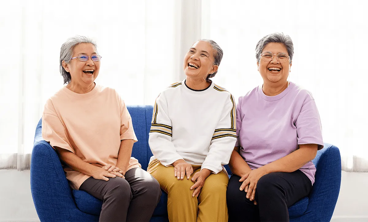Three seniors laughing together on a blue couch
