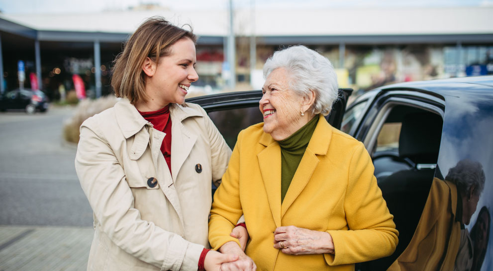 A caregiver greeting a smiling senior outside a building