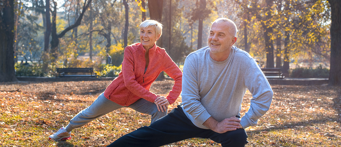 Two seniors stretching in a sunny park