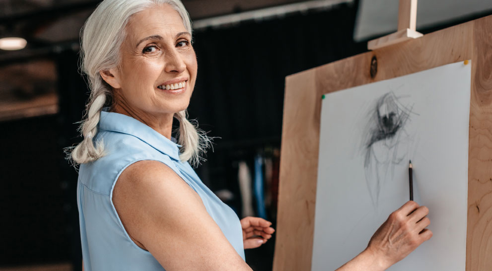 A senior woman drawing on a sketchpad in an activity room.