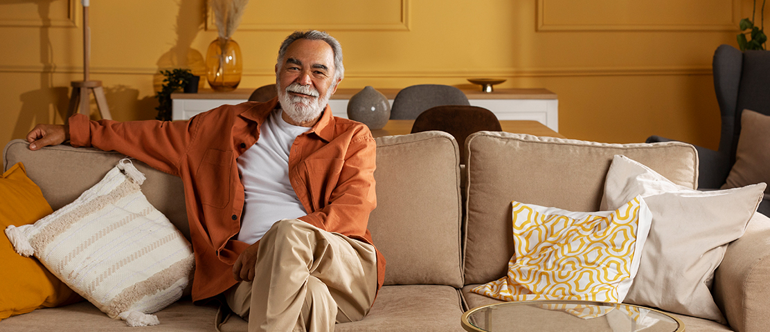 A smiling senior man sitting on a couch in a cozy living area