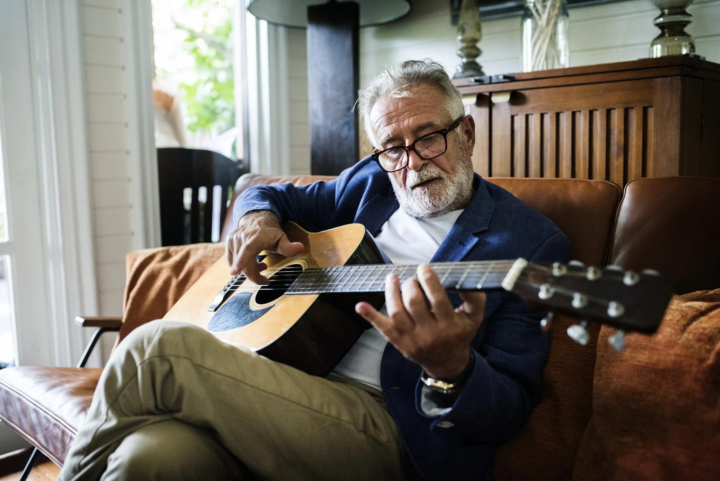 An elderly man playing guitar in a cozy indoor setting