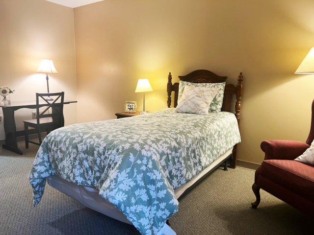 Cozy single bedroom with floral bedding and lamp.