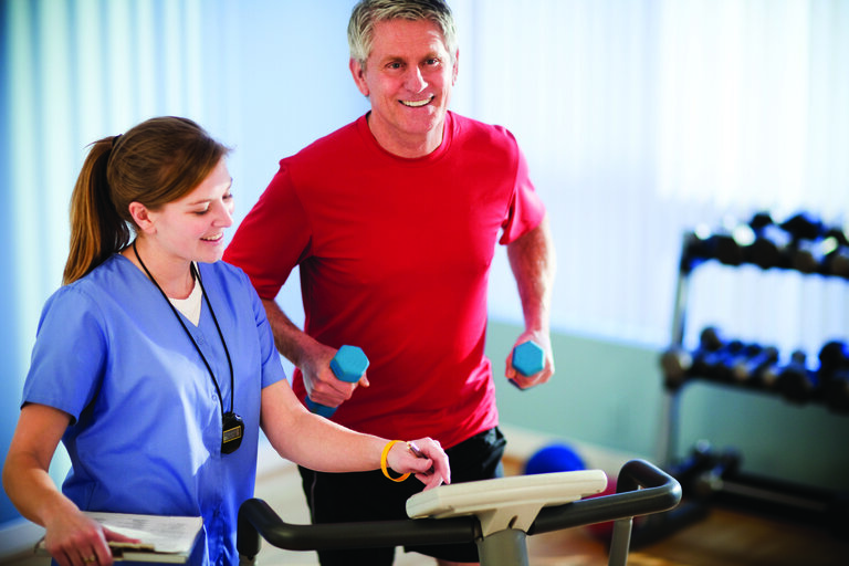 Senior man exercising with staff assistance indoors.