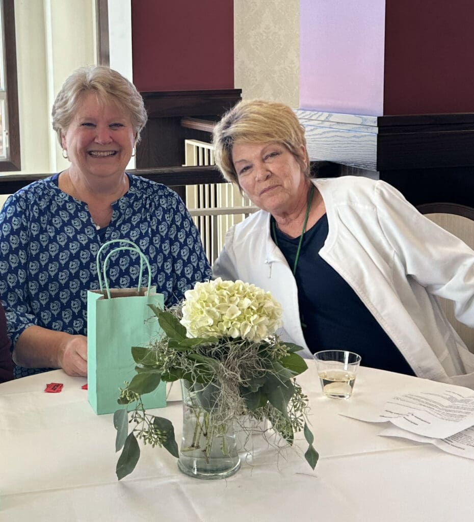 Two women smiling at a table with flowers.
