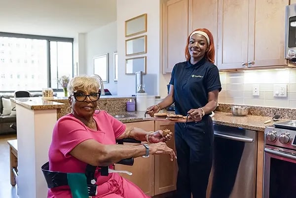 A resident and staff member in a kitchen preparing food.