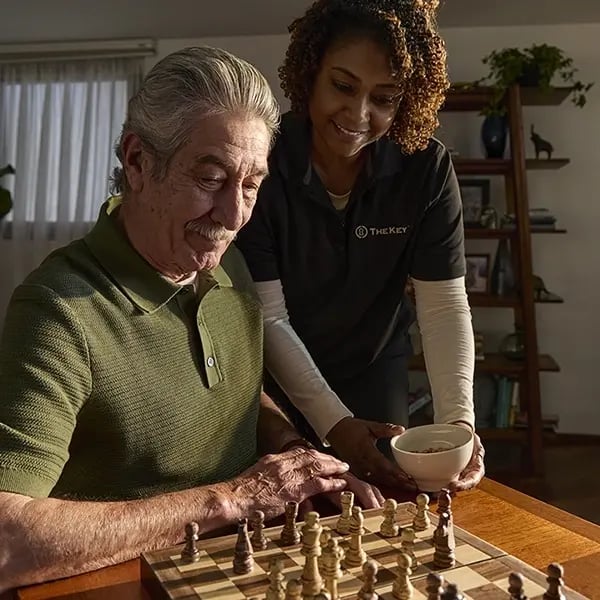 A caregiver assists a resident with chess.
