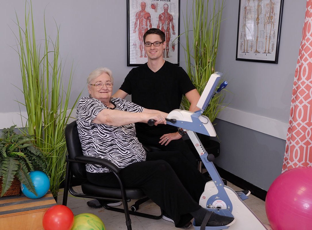 Senior resident using exercise equipment with staff assistance.