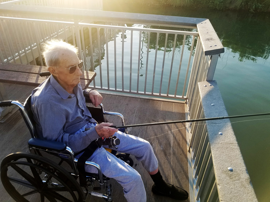 Elderly man in wheelchair fishing by the water.