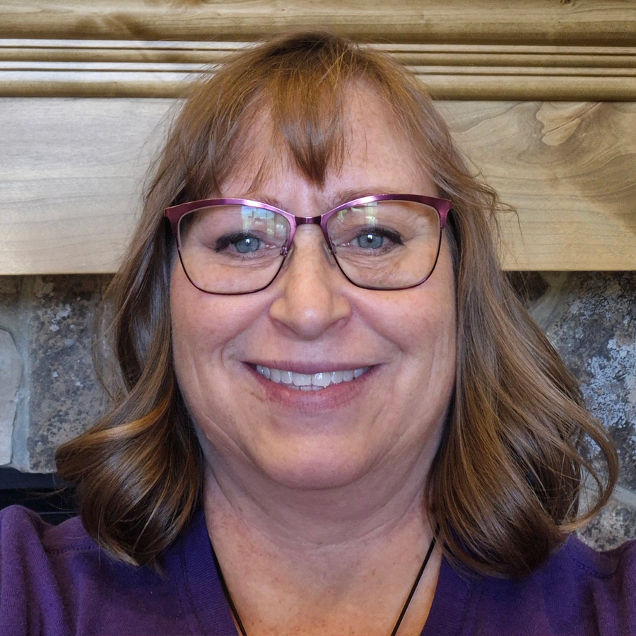 Smiling woman with glasses in front of a stone fireplace.