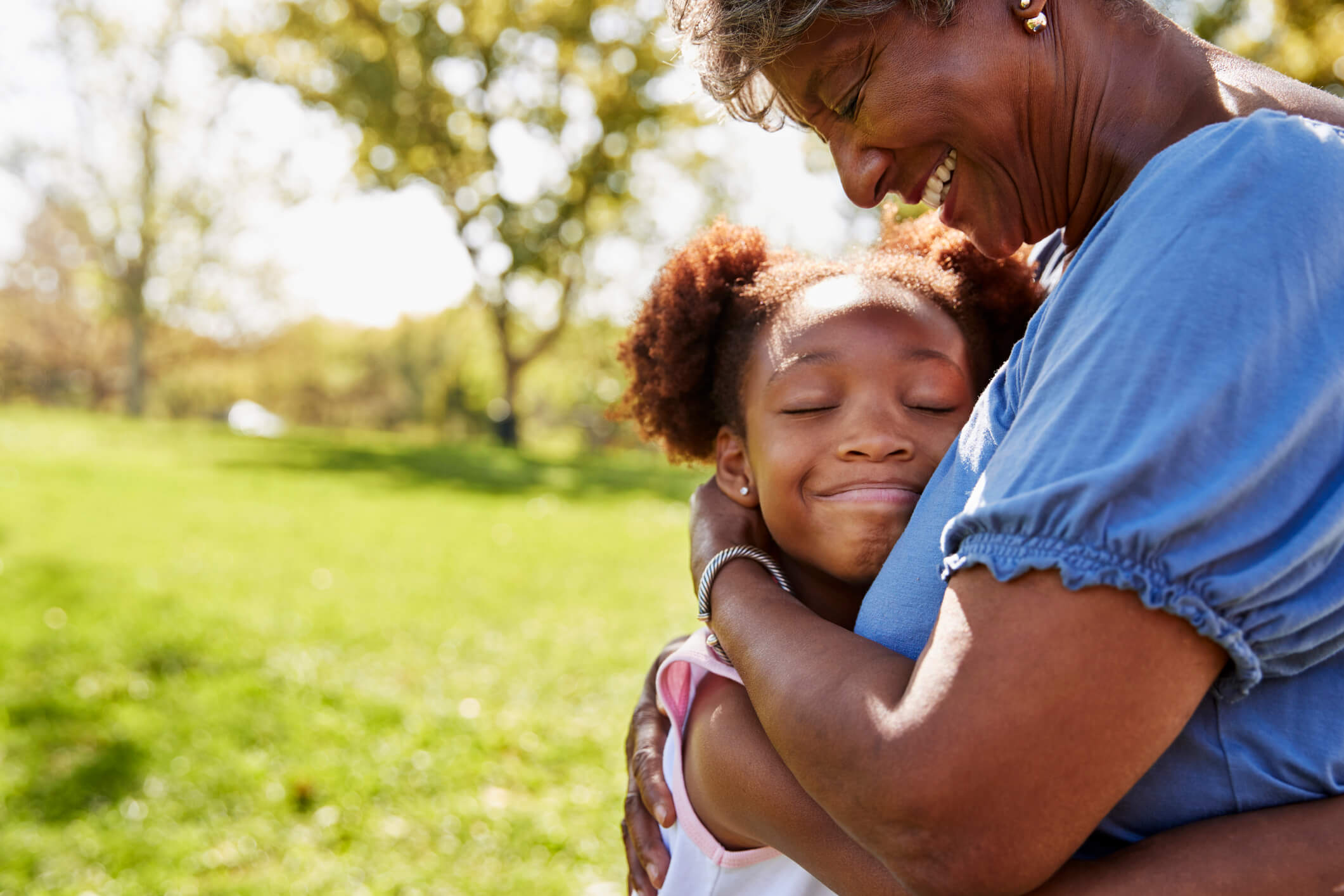 A senior woman embracing a young girl outside in a park