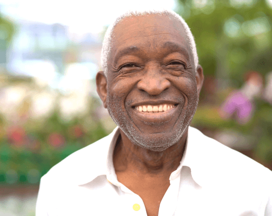 An elderly man smiling in a garden setting