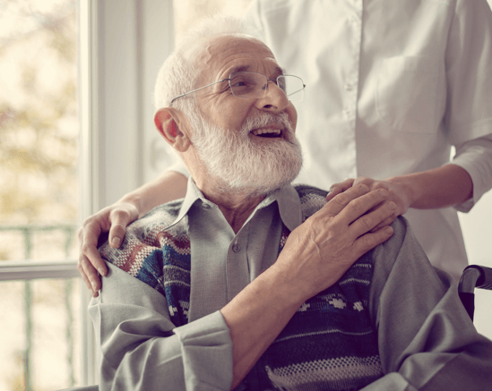 Elderly man smiling with caregiver in a bright indoor space