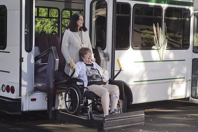 Resident in a wheelchair being assisted from a facility transport bus