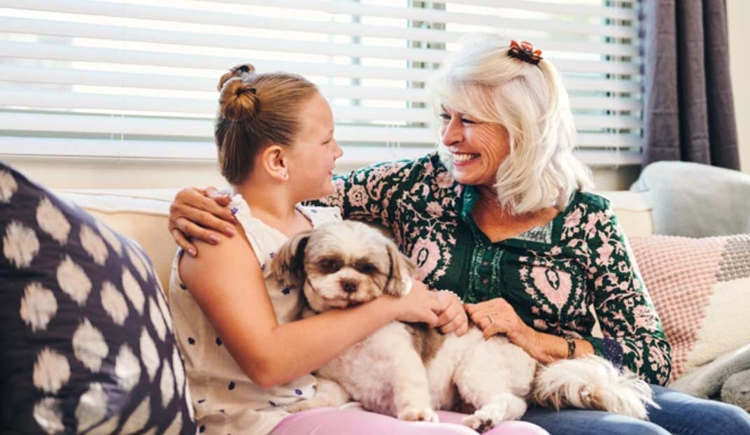 A resident and a child smiling with a dog on a couch