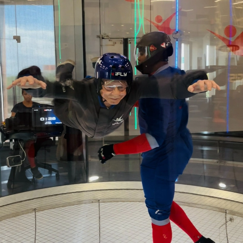 An older adult engaged in indoor skydiving with an instructor