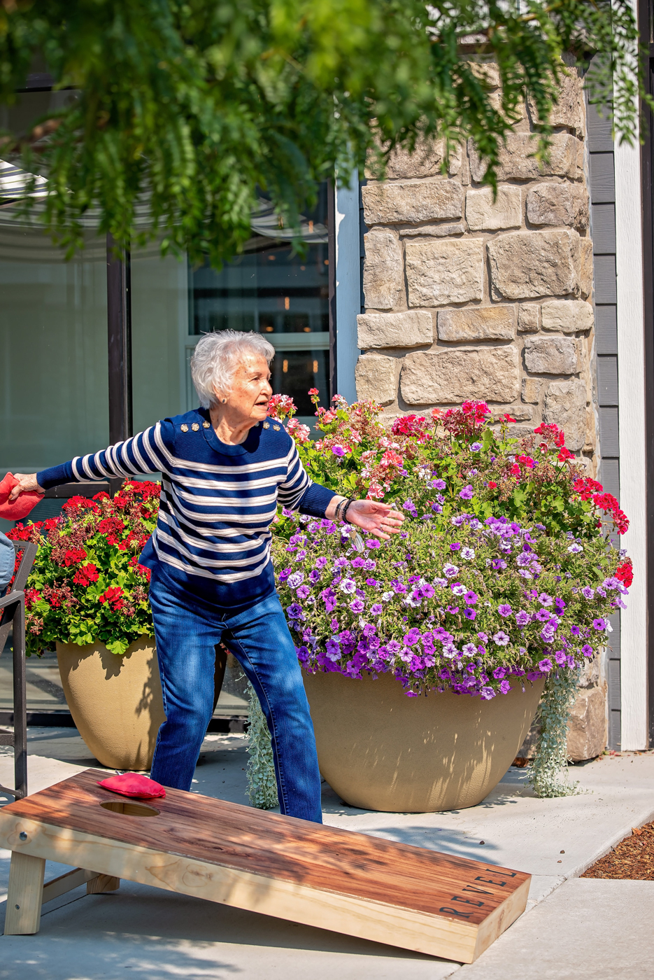 A senior playing cornhole outdoors with flower pots