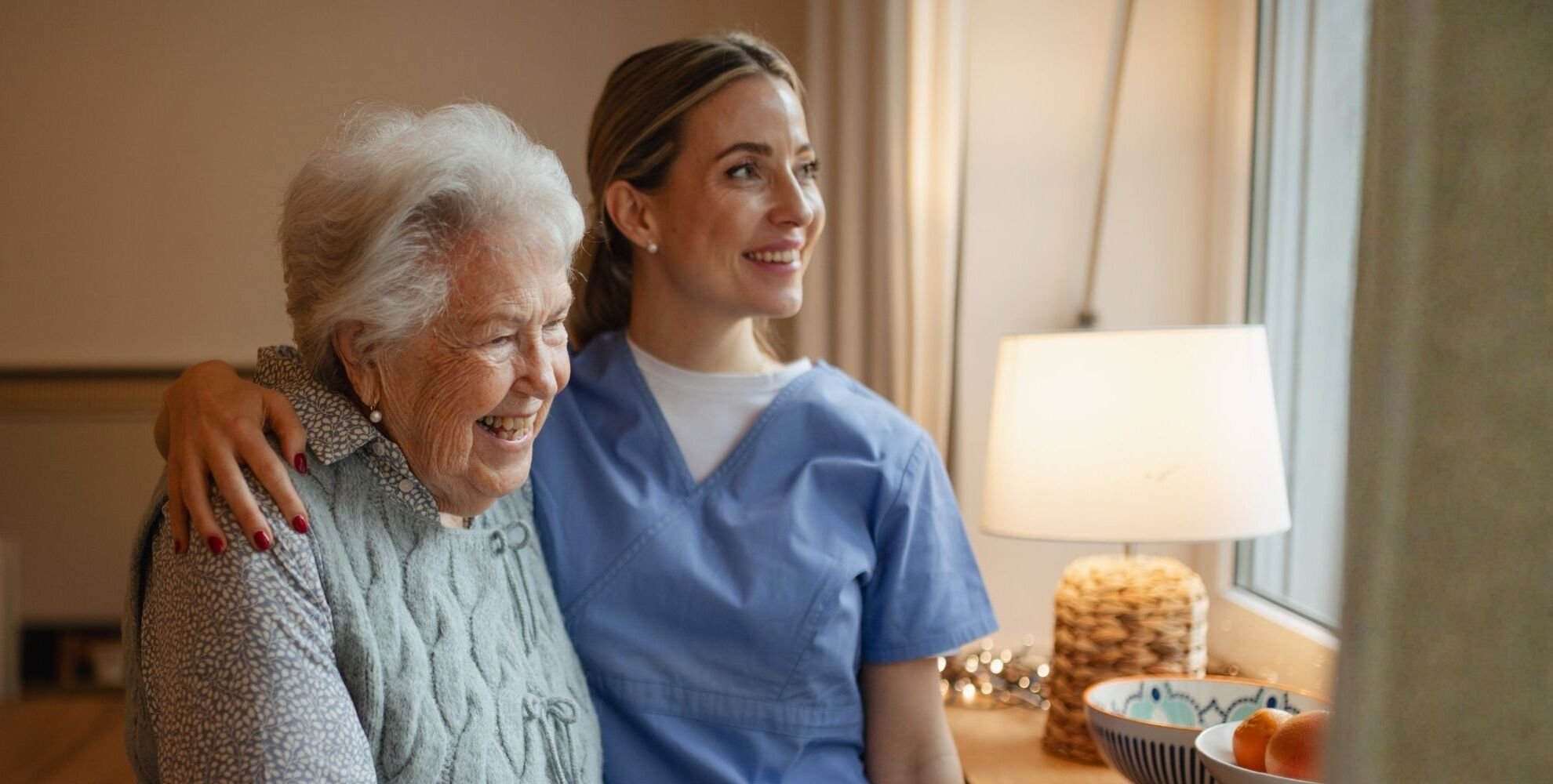 A caregiver and a resident smiling by a window