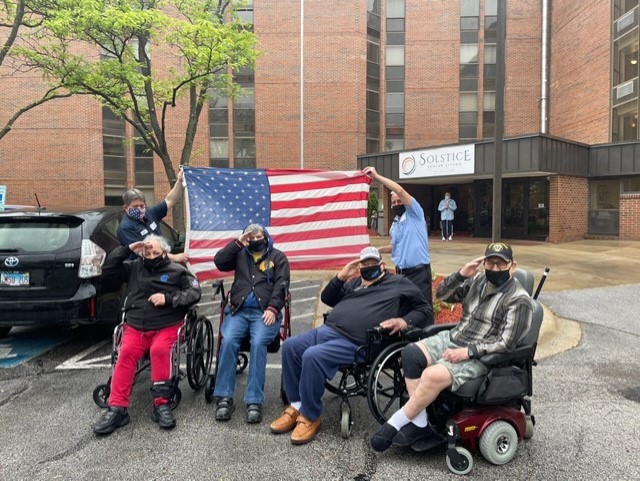 Residents saluting with an American flag in front of the facility