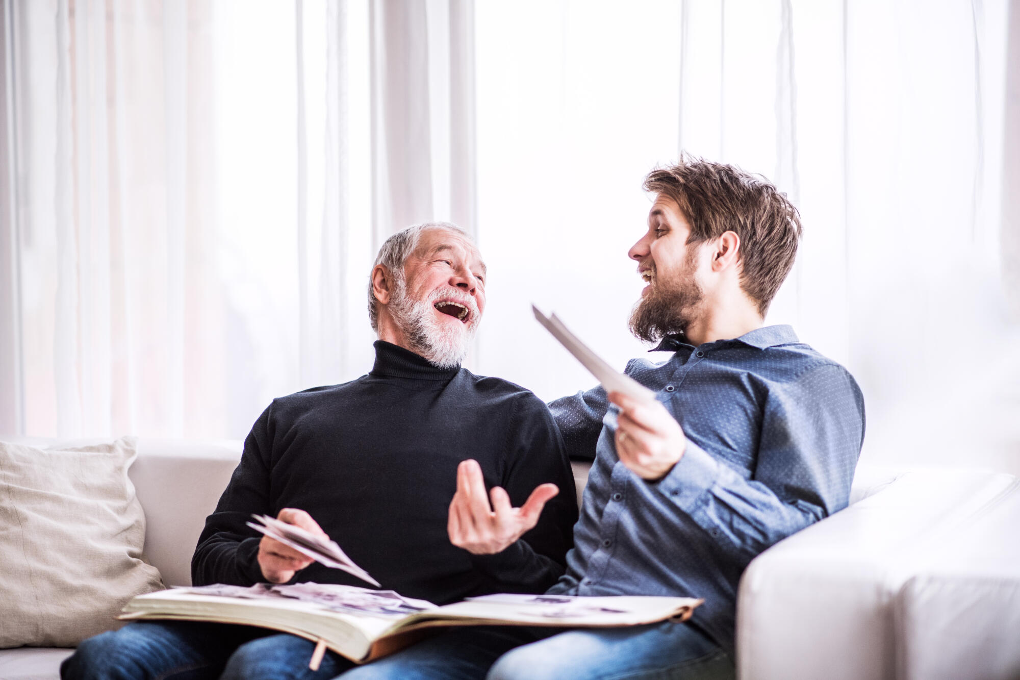 Two men laughing while looking at a photo album on a couch