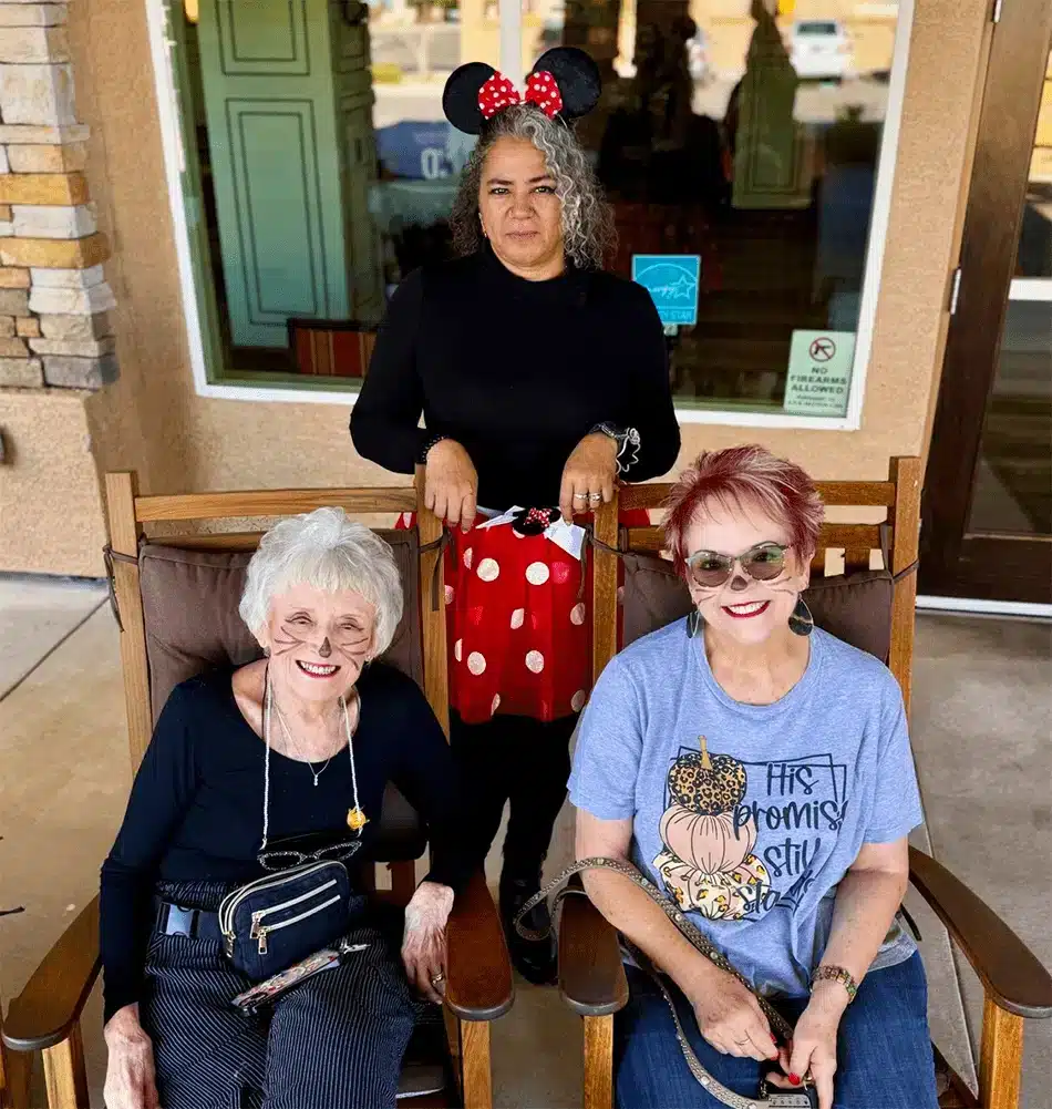 Three residents and staff smiling outdoors in a courtyard