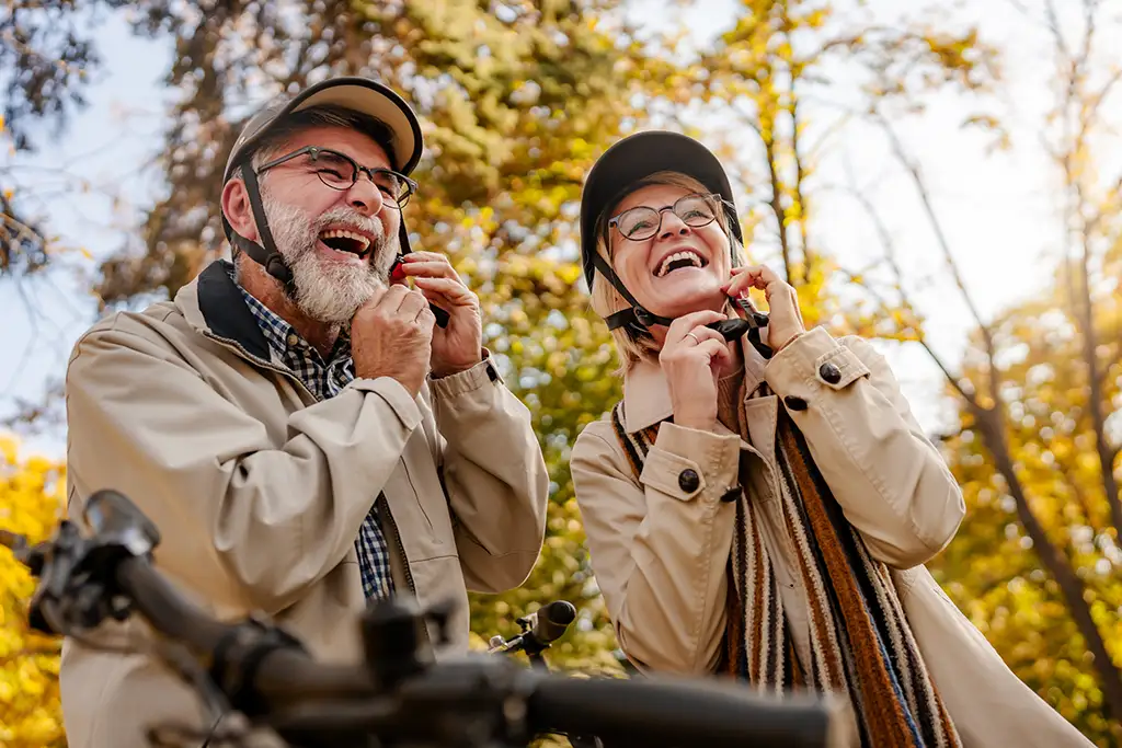 Two seniors smiling outdoors wearing helmets