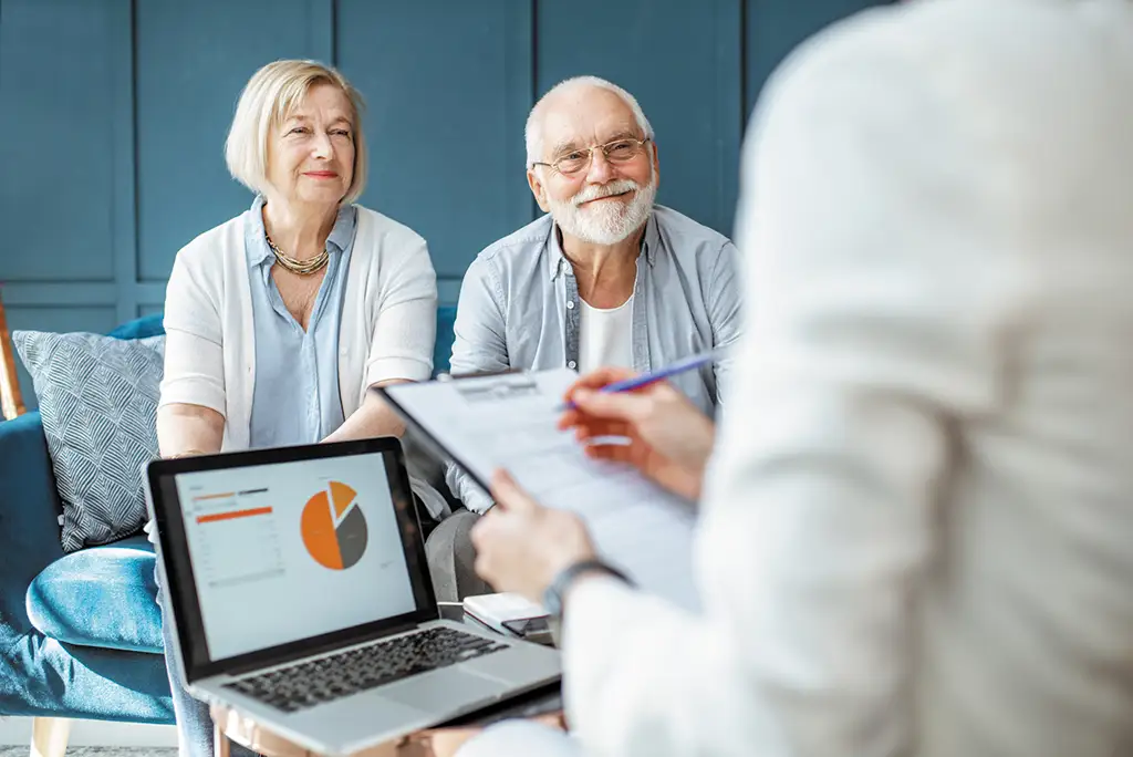 Elderly couple consulting with a staff member, laptop visible