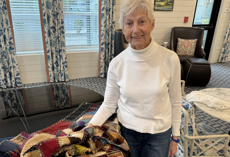Senior resident showcasing a colorful quilt in a common area