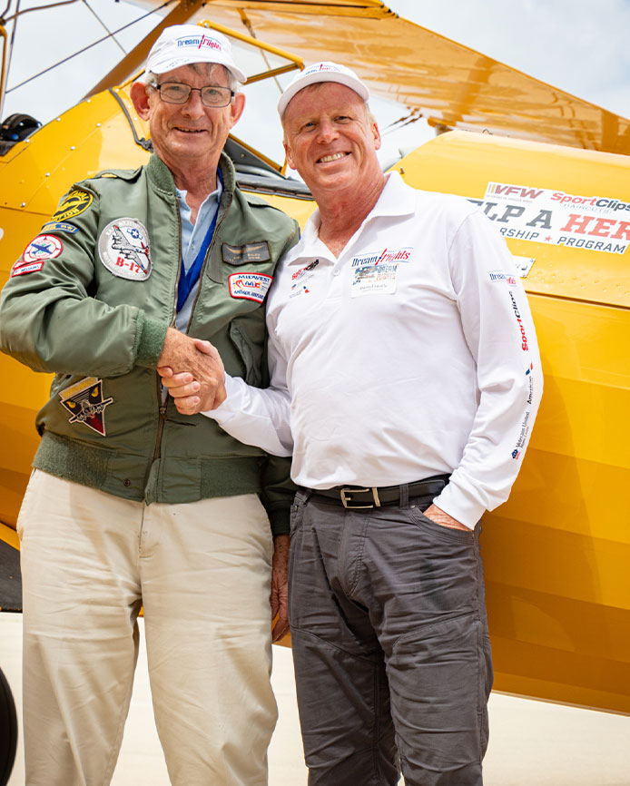 Two men shaking hands in front of a vintage aircraft