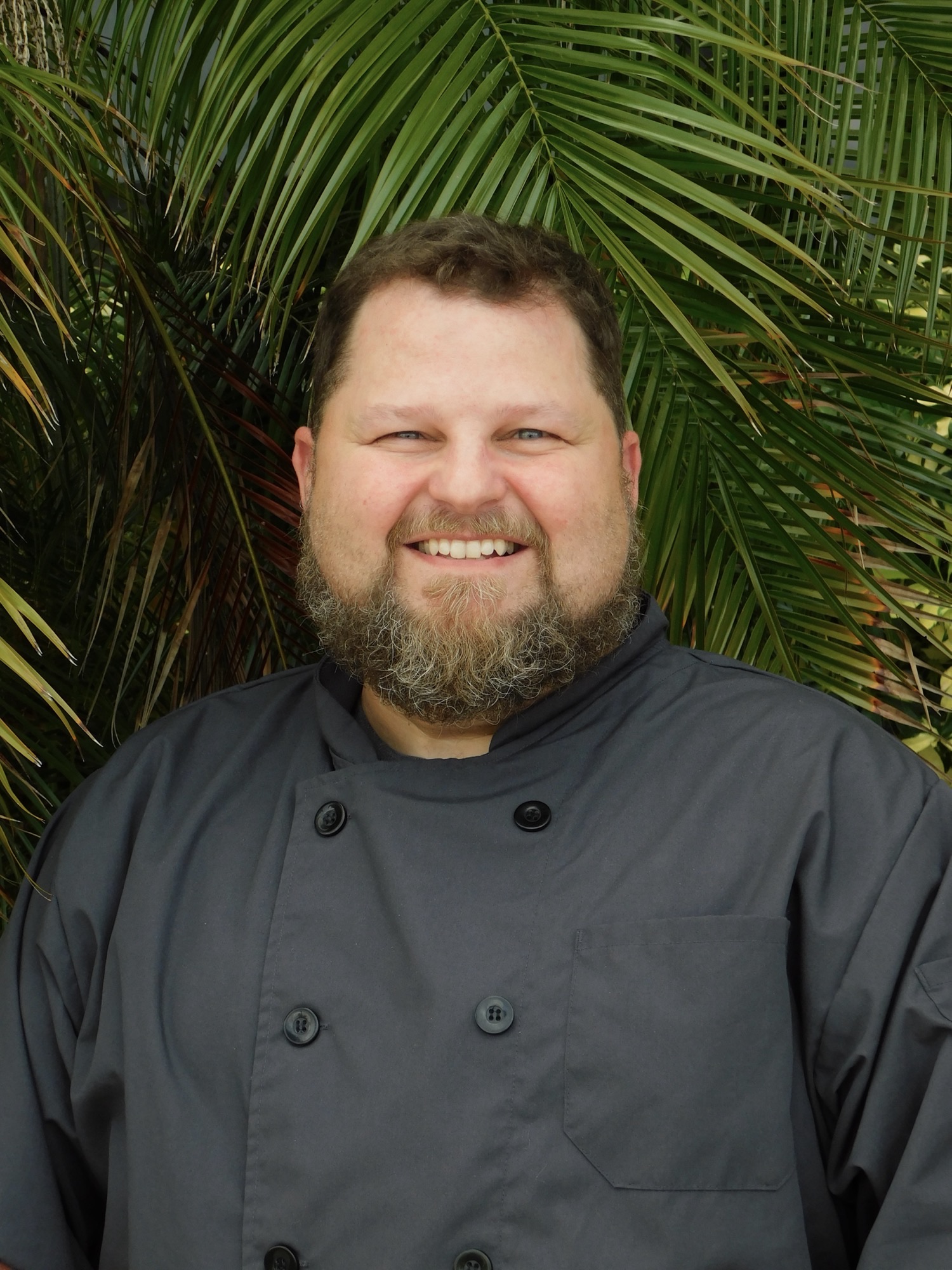 Chef smiling in front of tropical plants
