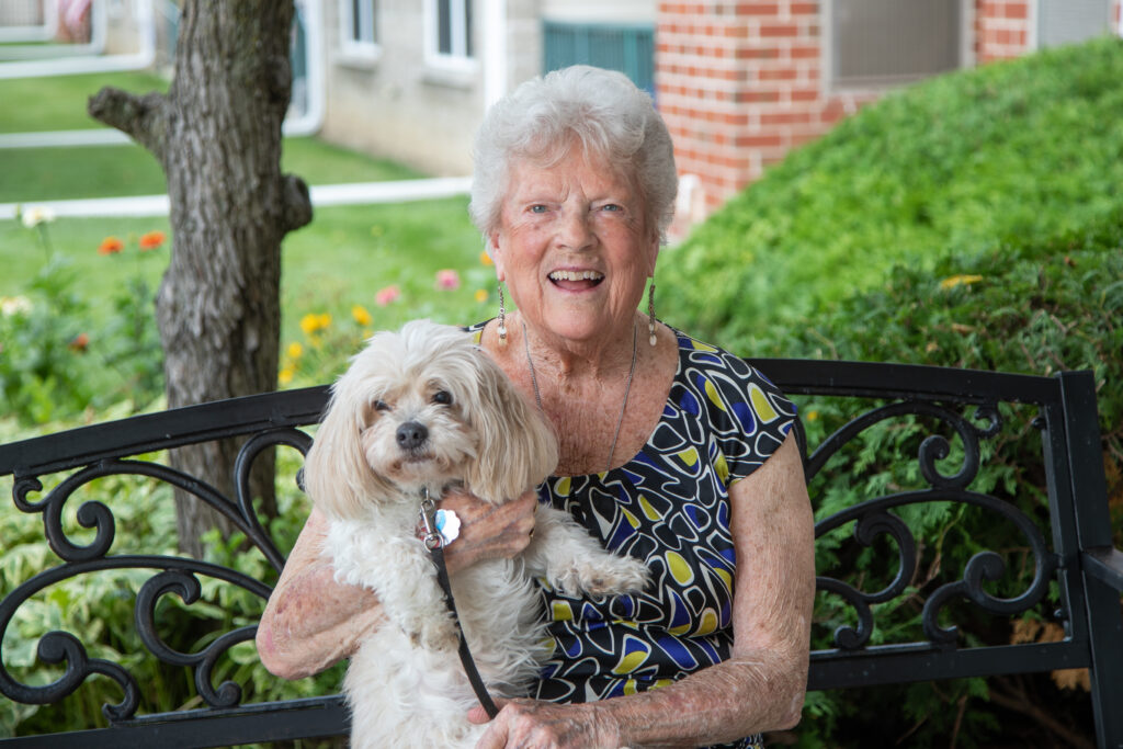 Smiling resident holding a small dog on a bench