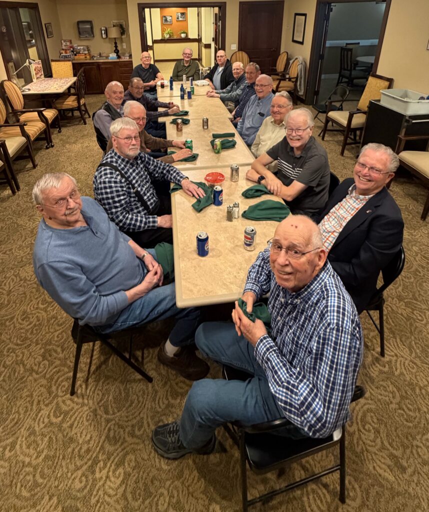 Group of older men gathered around a table in a common area