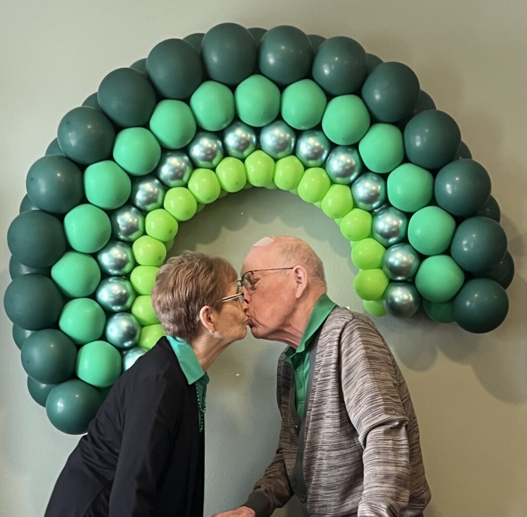 Couple sharing a kiss in front of a balloon rainbow