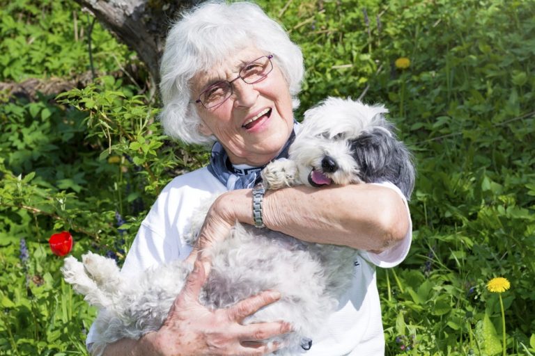 Senior resident happily holding a dog outdoors