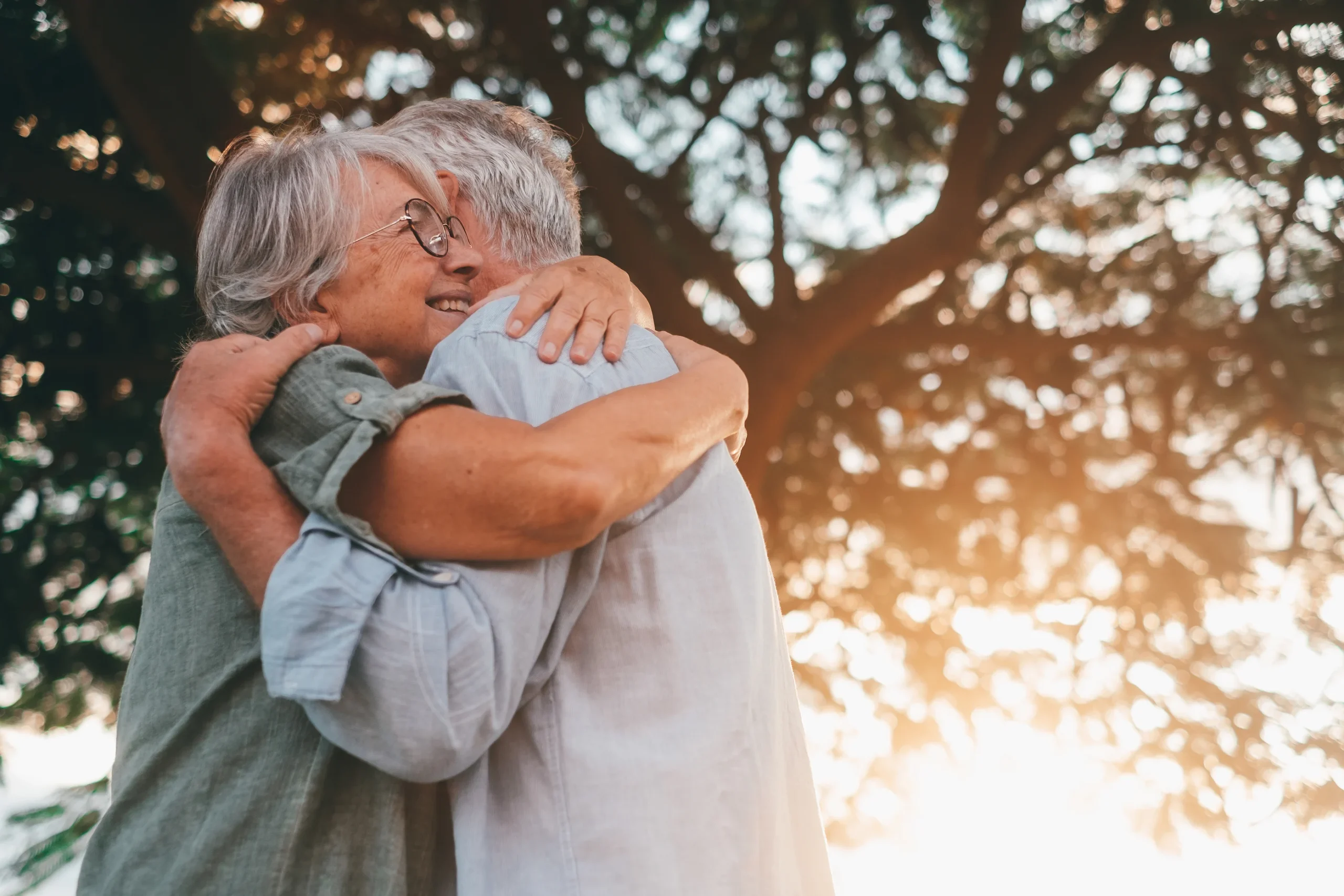 Two seniors embracing outdoors under a tree